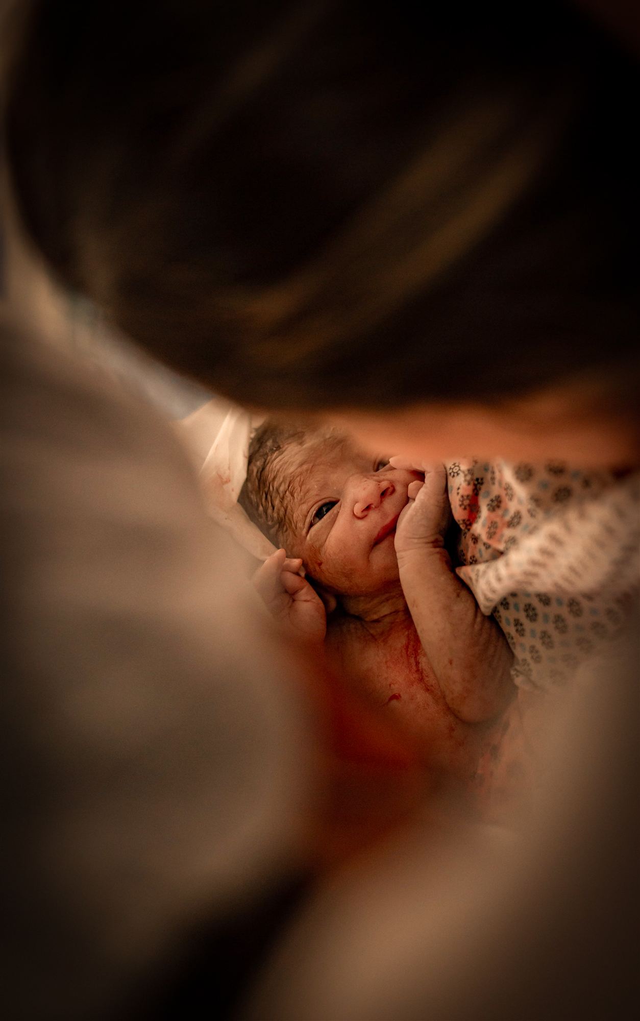 Recém-nascido olhando para a mãe, visto por entre os braços dela